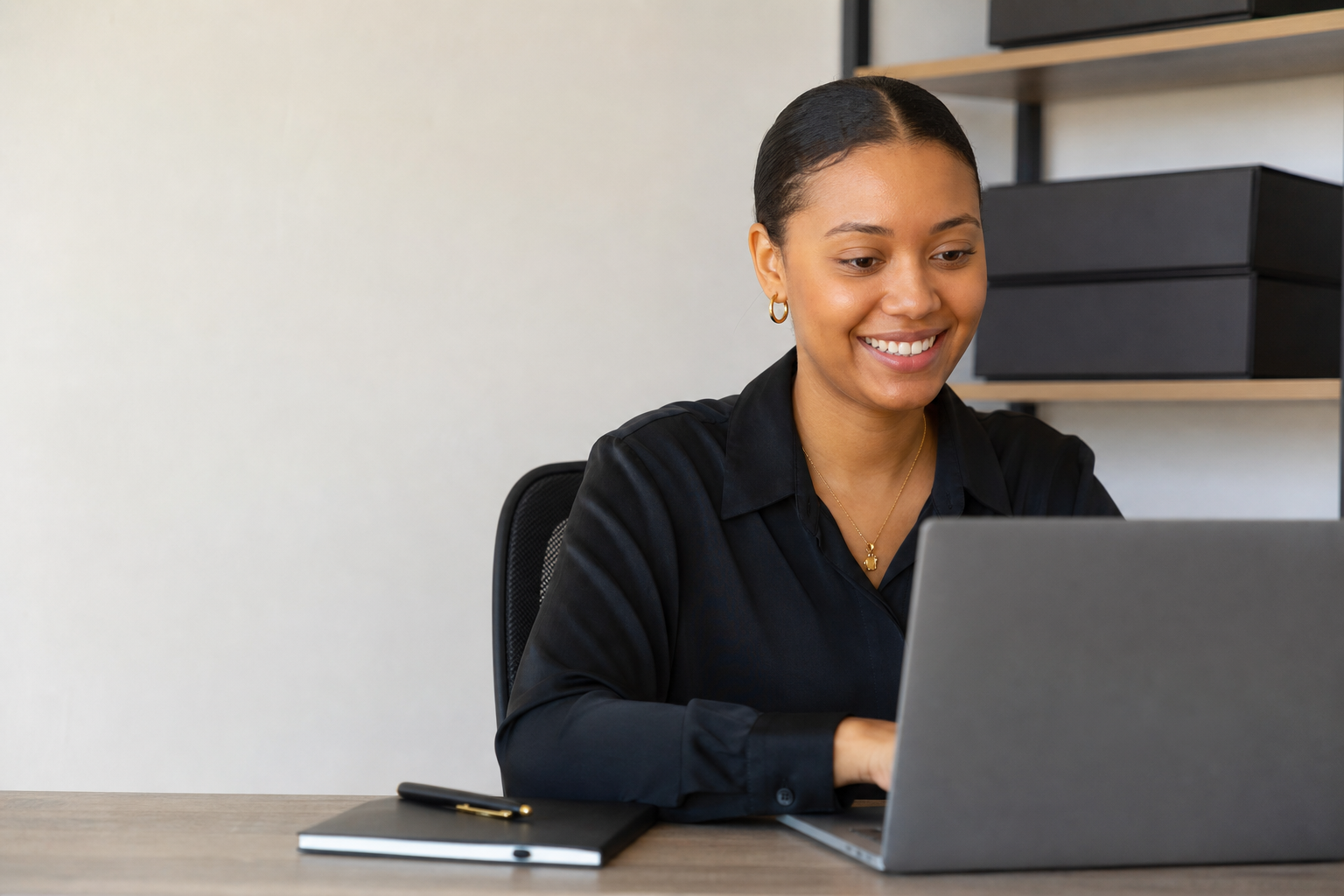 A MokiHair team member working at her laptop with ready-to-sell wigs professionally packaged behind her